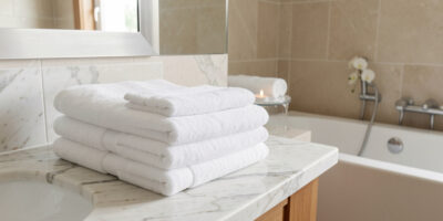Folded white towels neatly stacked on a marble bathroom countertop with bathtub in background
