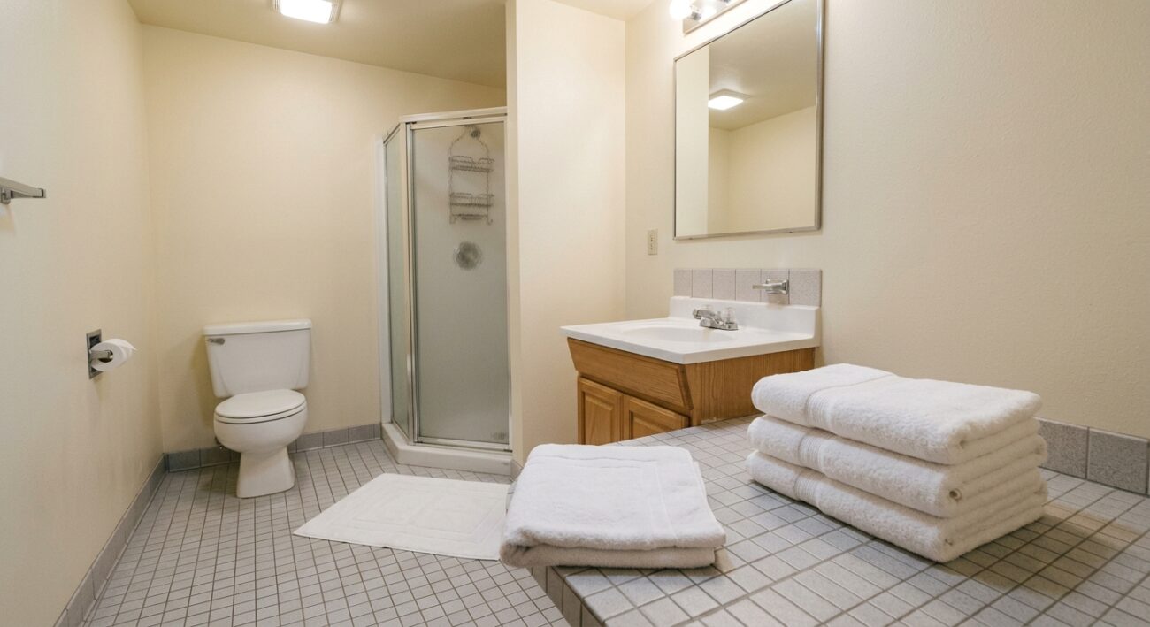 Simple motel bathroom with a folded white towel and matching bath mat on tiled floor, practical and clean lighting, no people